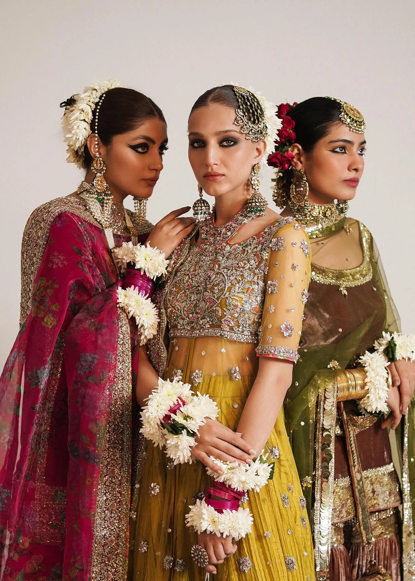 Three women in traditional embroidered dresses with jewelry and floral accessories.