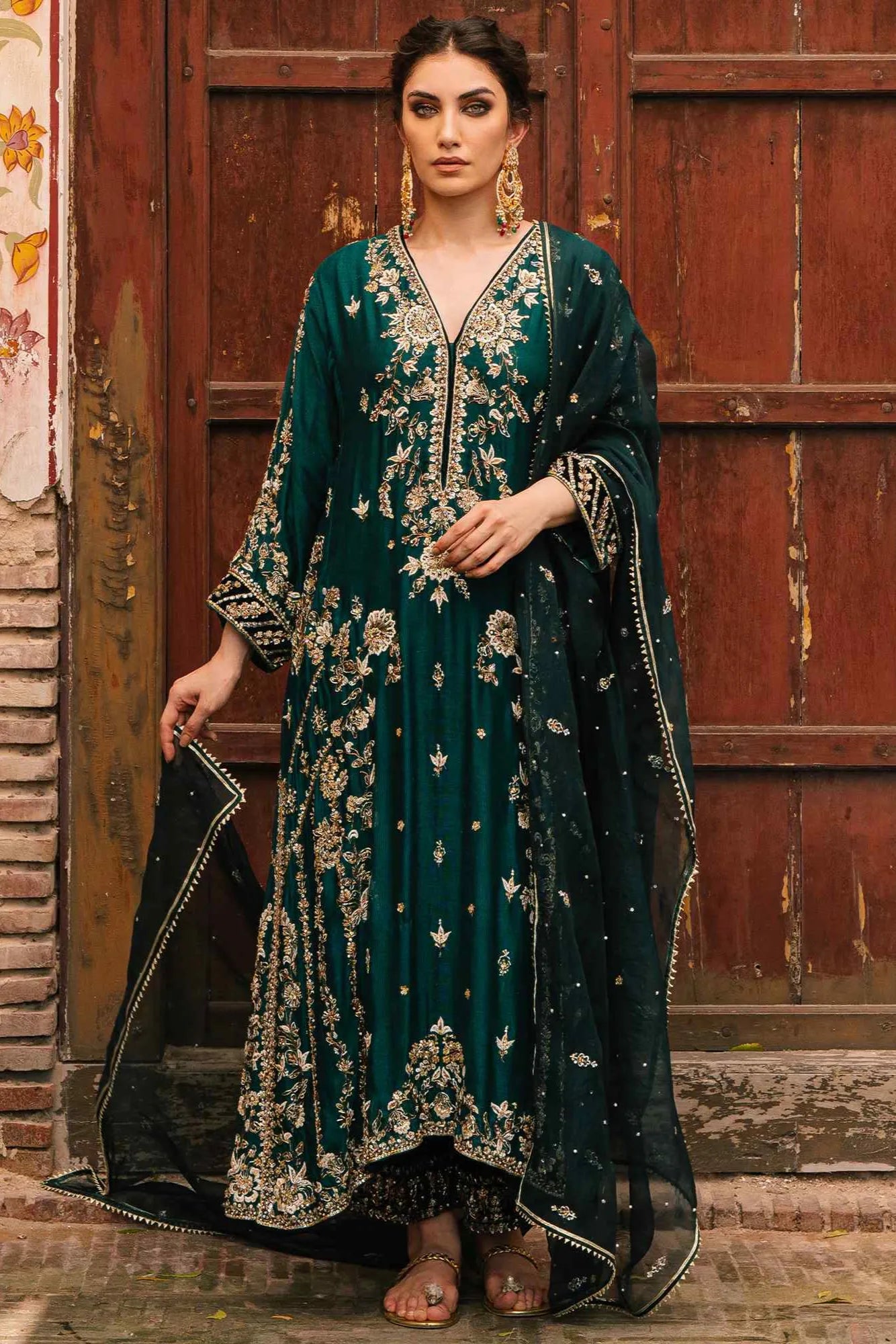 Woman in a dark green embroidered traditional outfit standing in front of a wooden door.