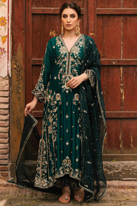 Woman in a dark green embroidered traditional outfit standing in front of a wooden door.