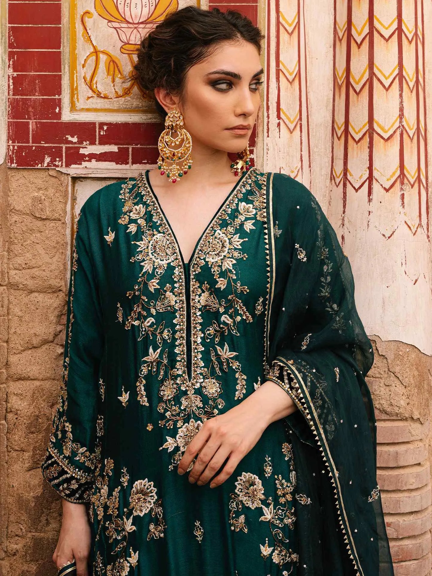 Woman in a green embroidered traditional outfit standing against a textured wall.