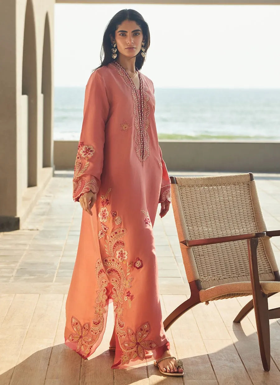 Woman in a peach embroidered outfit standing on a wooden deck with ocean view