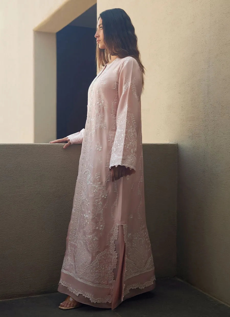 Woman in a light pink embroidered dress standing in a minimalistic room.