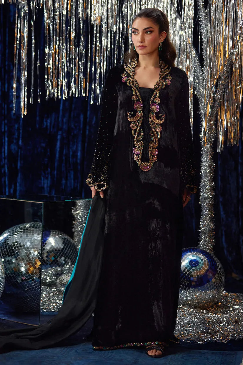 Woman in a black evening gown with intricate detailing against a glittery curtain backdrop.
