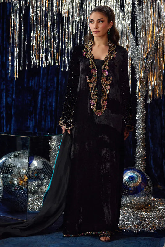 Woman in a black evening gown with intricate detailing against a glittery curtain backdrop.
