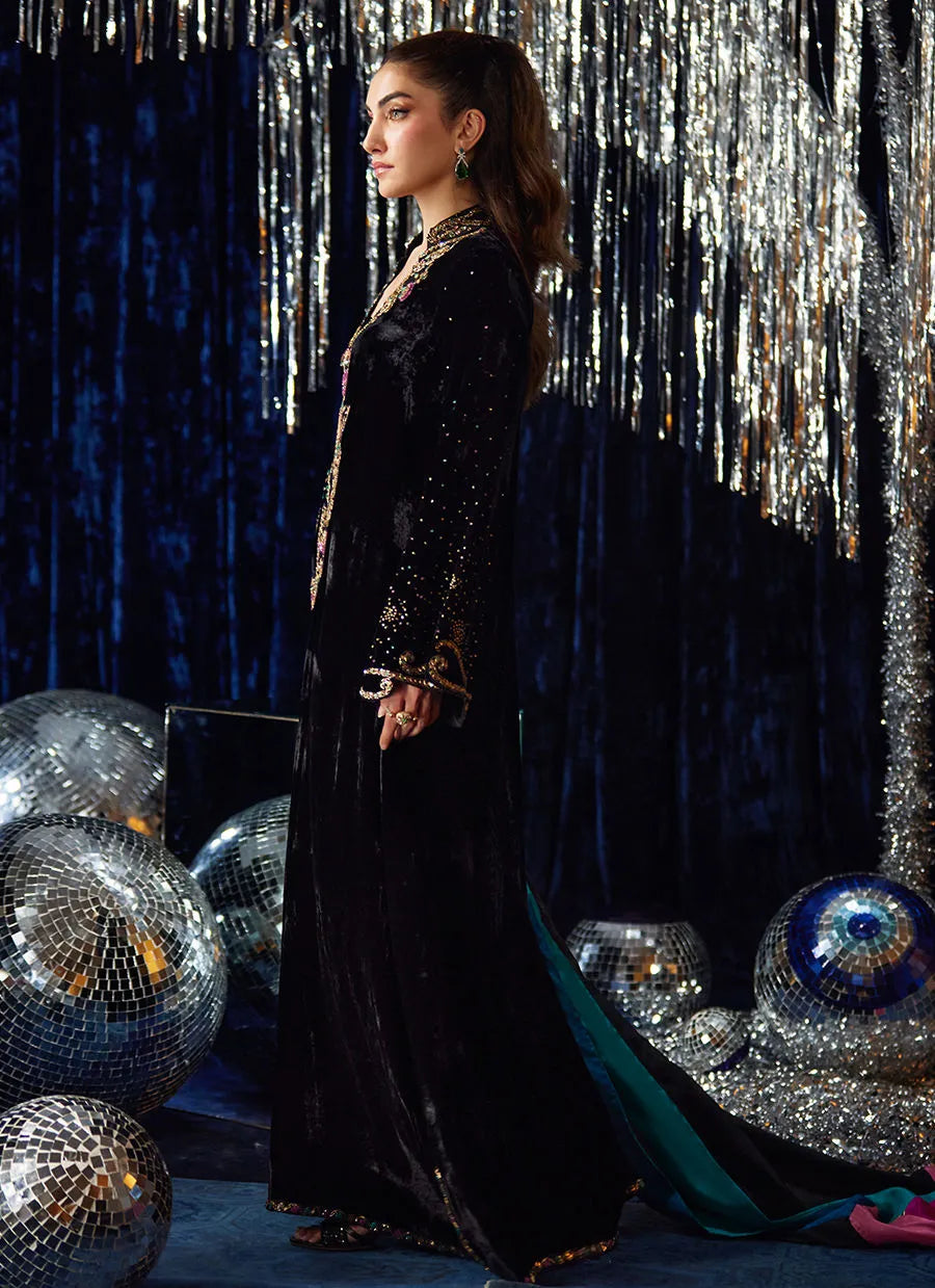 Woman in a black sequined outfit standing in front of disco balls and a silver curtain.