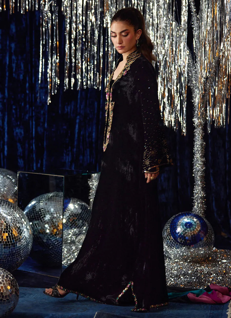 Woman in a black evening gown with gold accents standing against a festive background with disco balls and tinsel.