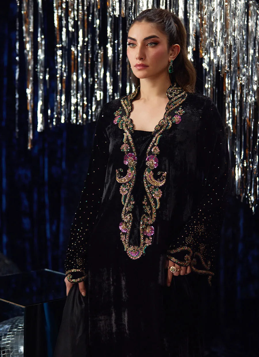 Woman wearing an ornate black outfit with embroidery against a reflective silver curtain background