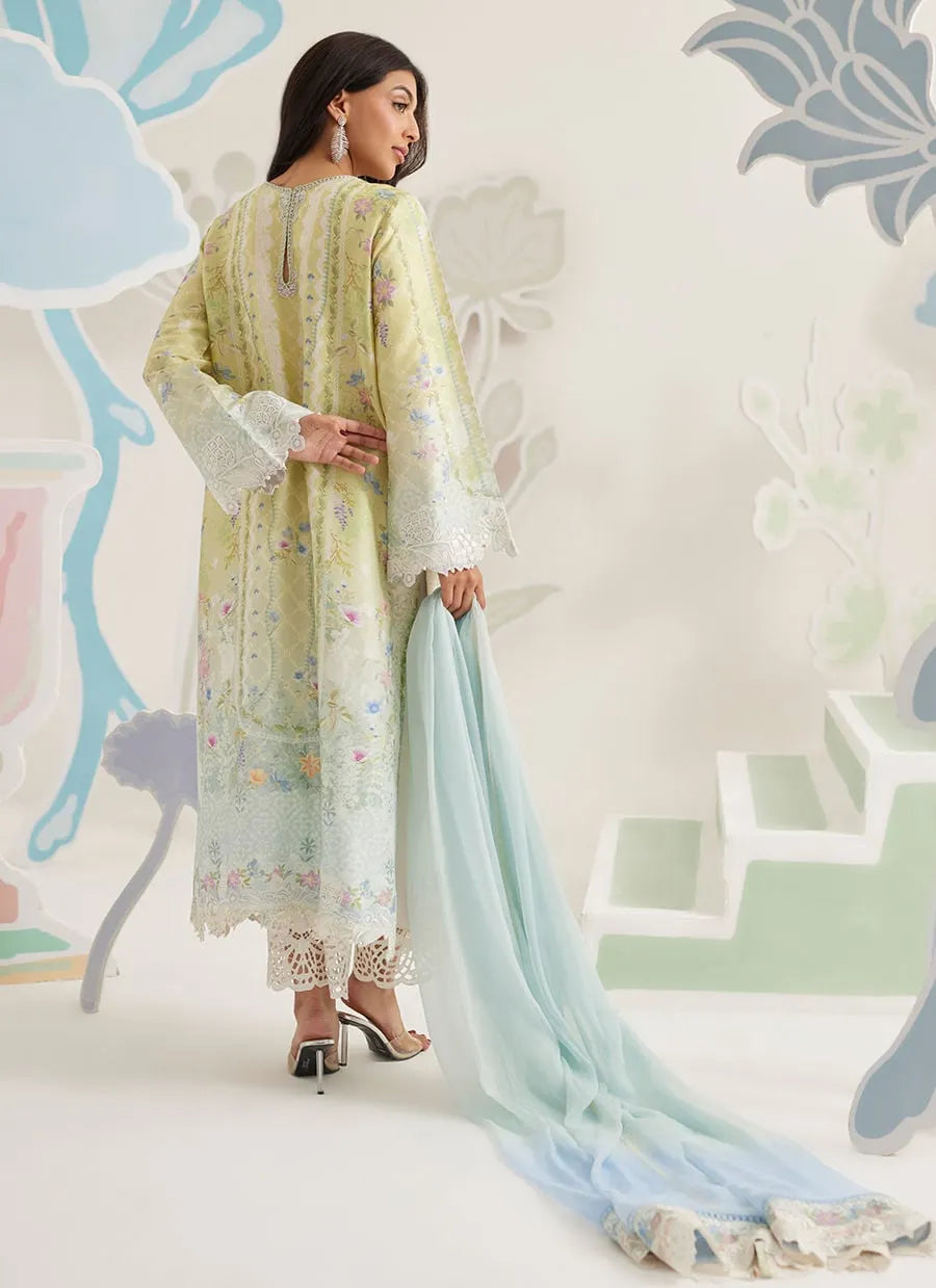Woman in a light green traditional outfit with a blue dupatta against a decorative wall.