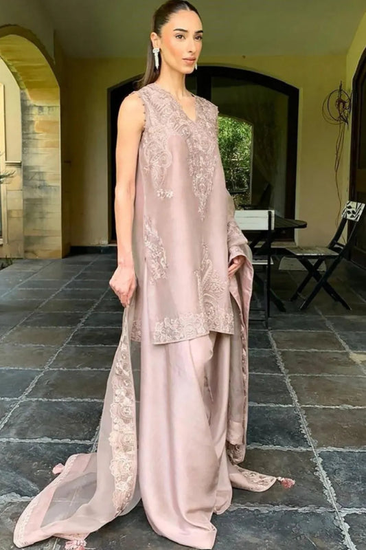 Woman in a light pink traditional outfit standing outdoors on a stone patio.