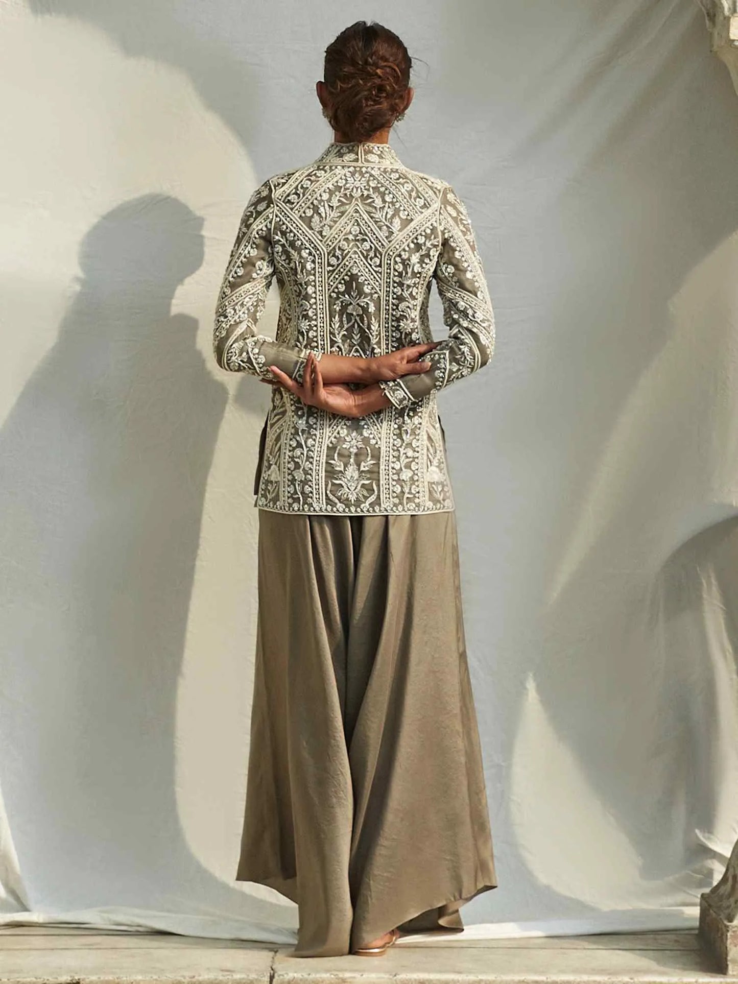 Person wearing an embroidered traditional outfit with a plain background