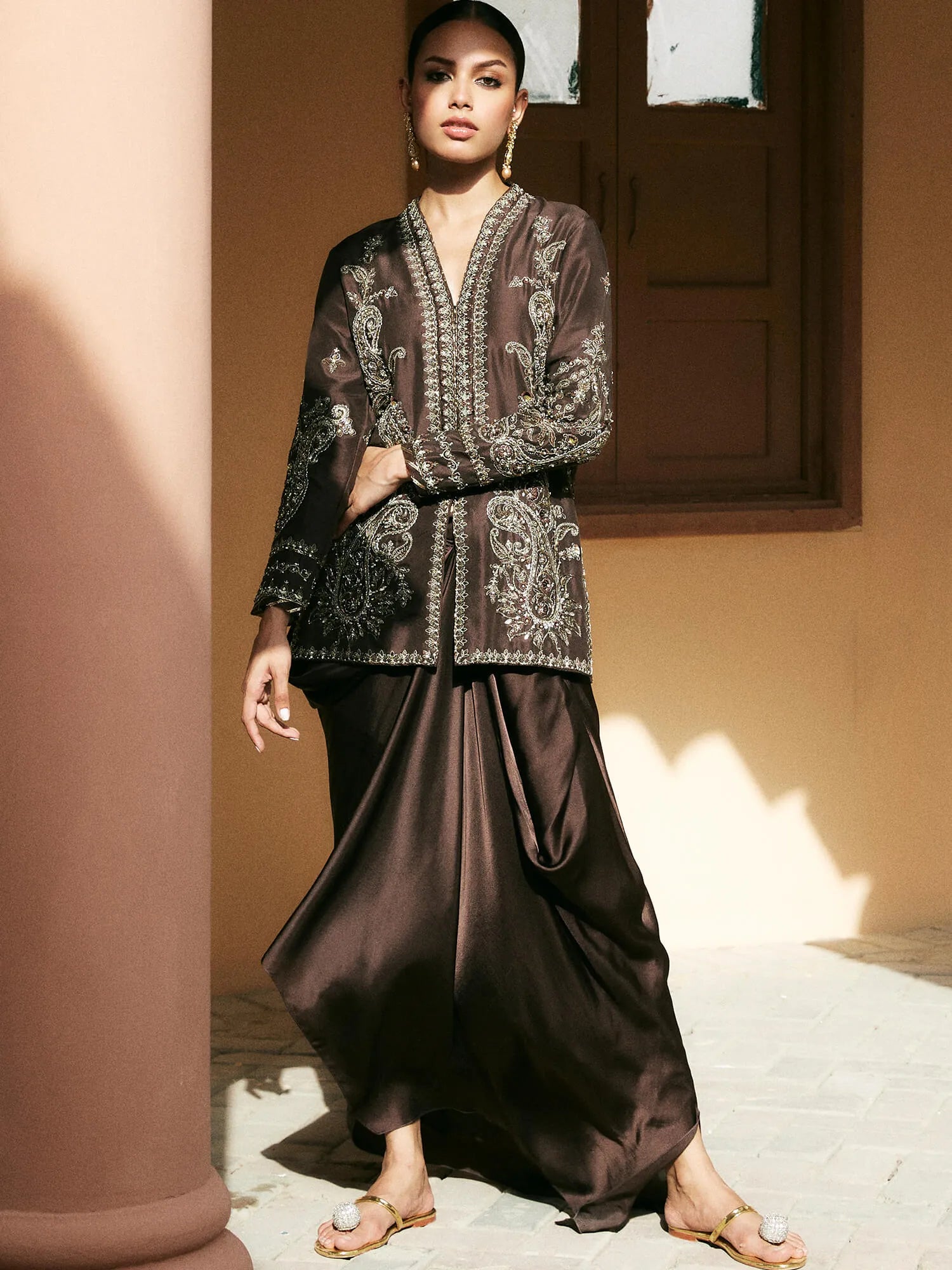 Woman wearing a traditional outfit with intricate patterns in a warm-toned setting
