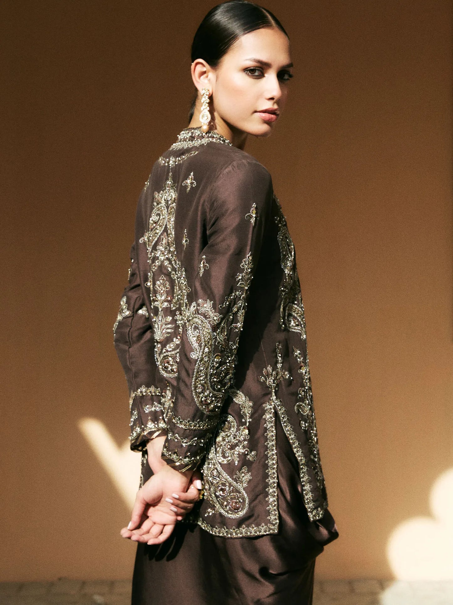 Woman wearing a dark brown embroidered top against a beige background