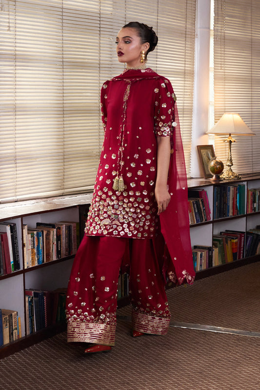 Woman in a red traditional outfit standing in a room with bookshelves.