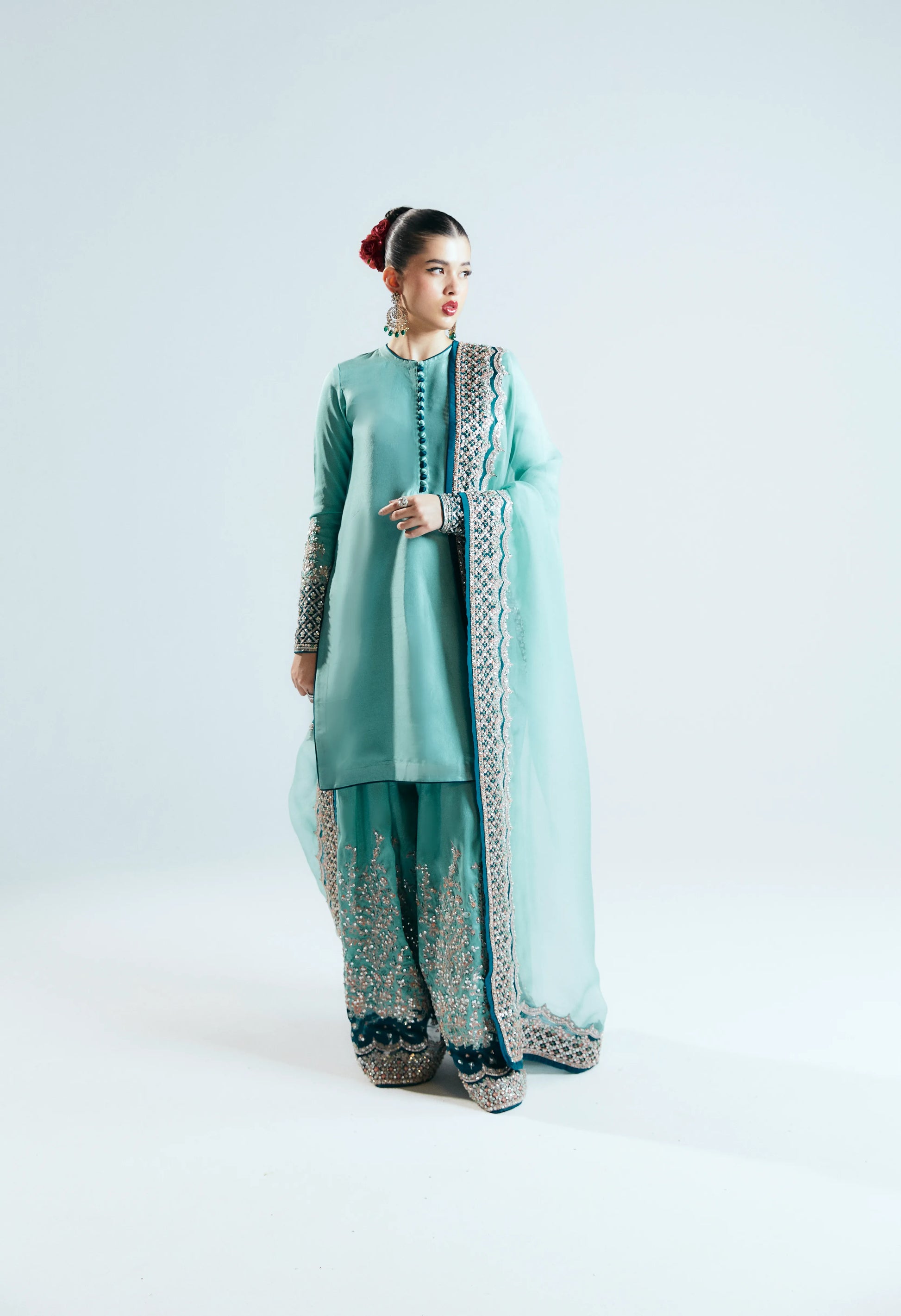 Woman wearing a light blue traditional outfit with intricate patterns on a white background