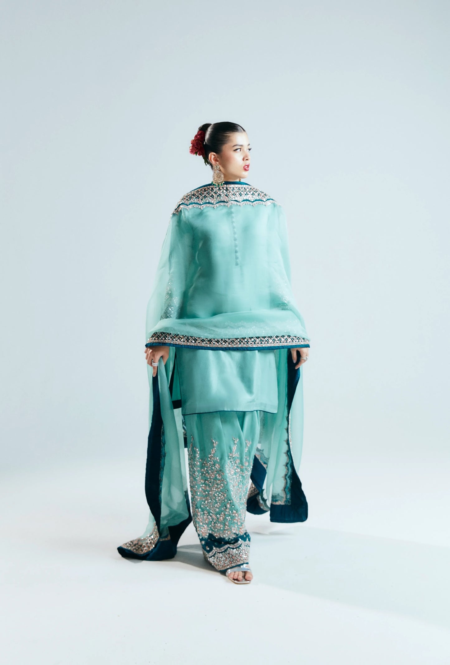 Woman wearing a traditional outfit with a light blue top and patterned pants on a white background