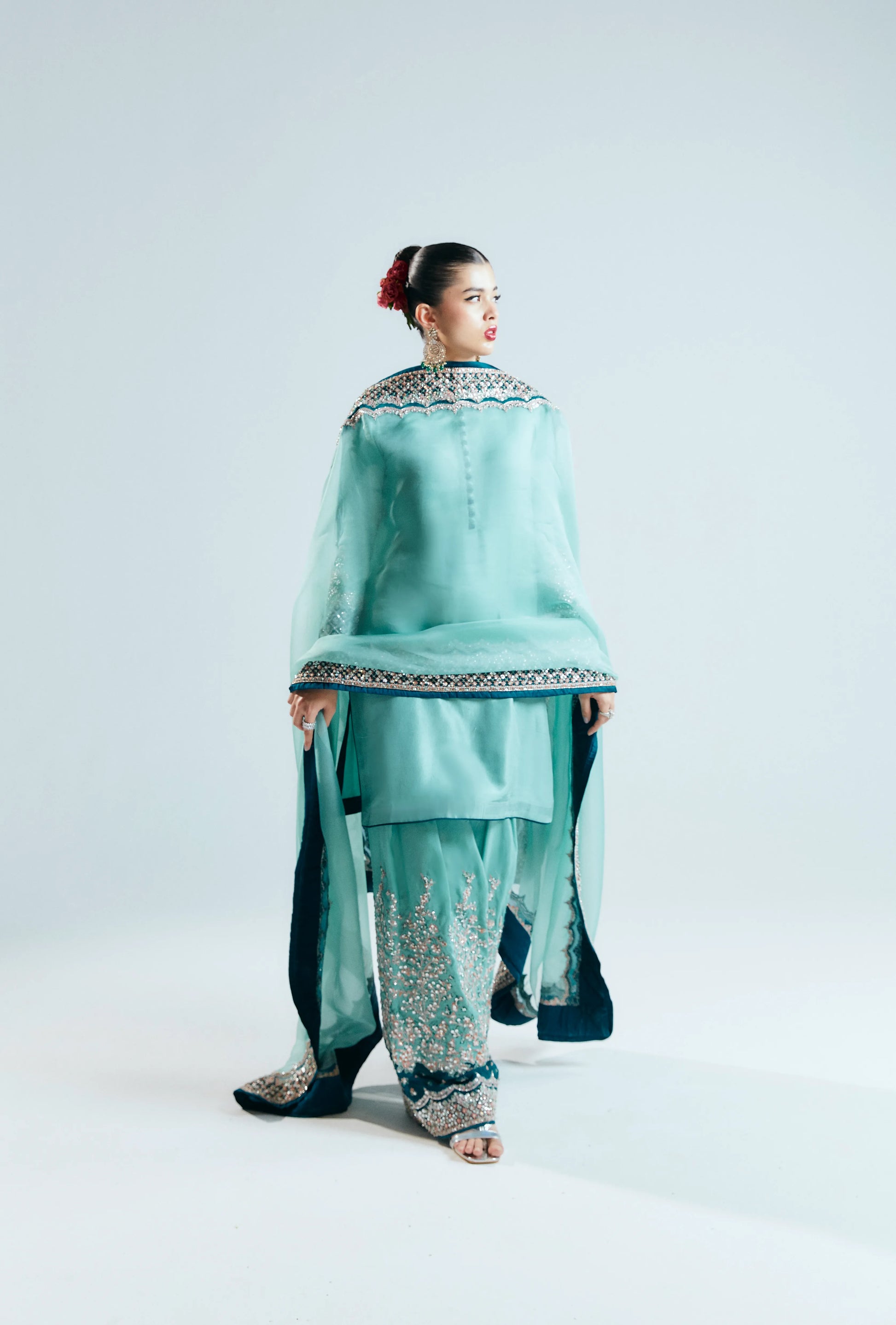 Woman wearing a traditional outfit with a light blue top and patterned pants on a white background