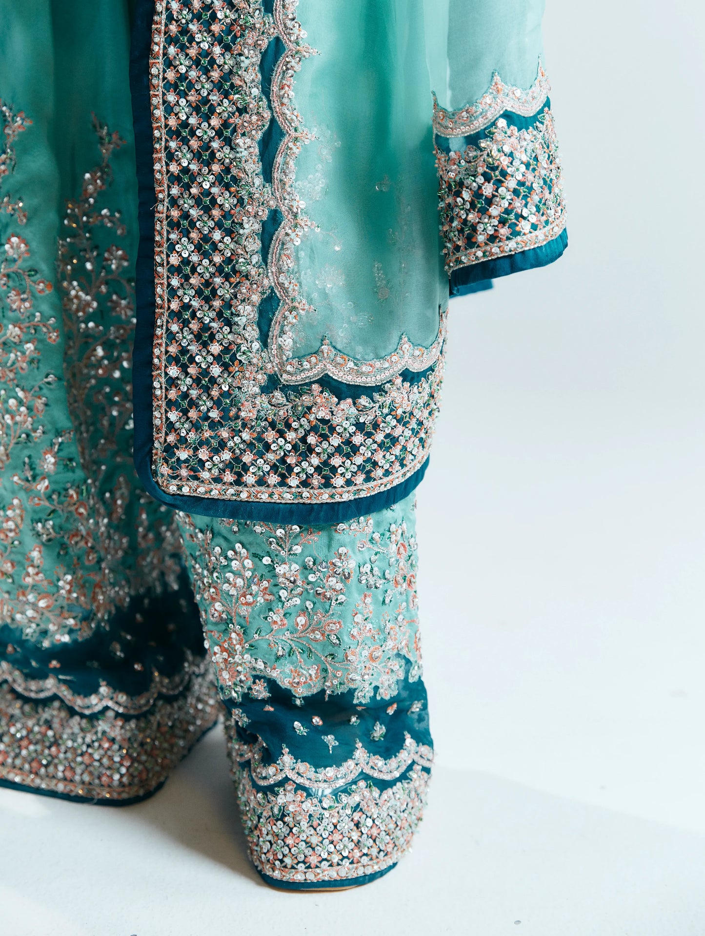 Teal traditional outfit with intricate silver embroidery on a white background