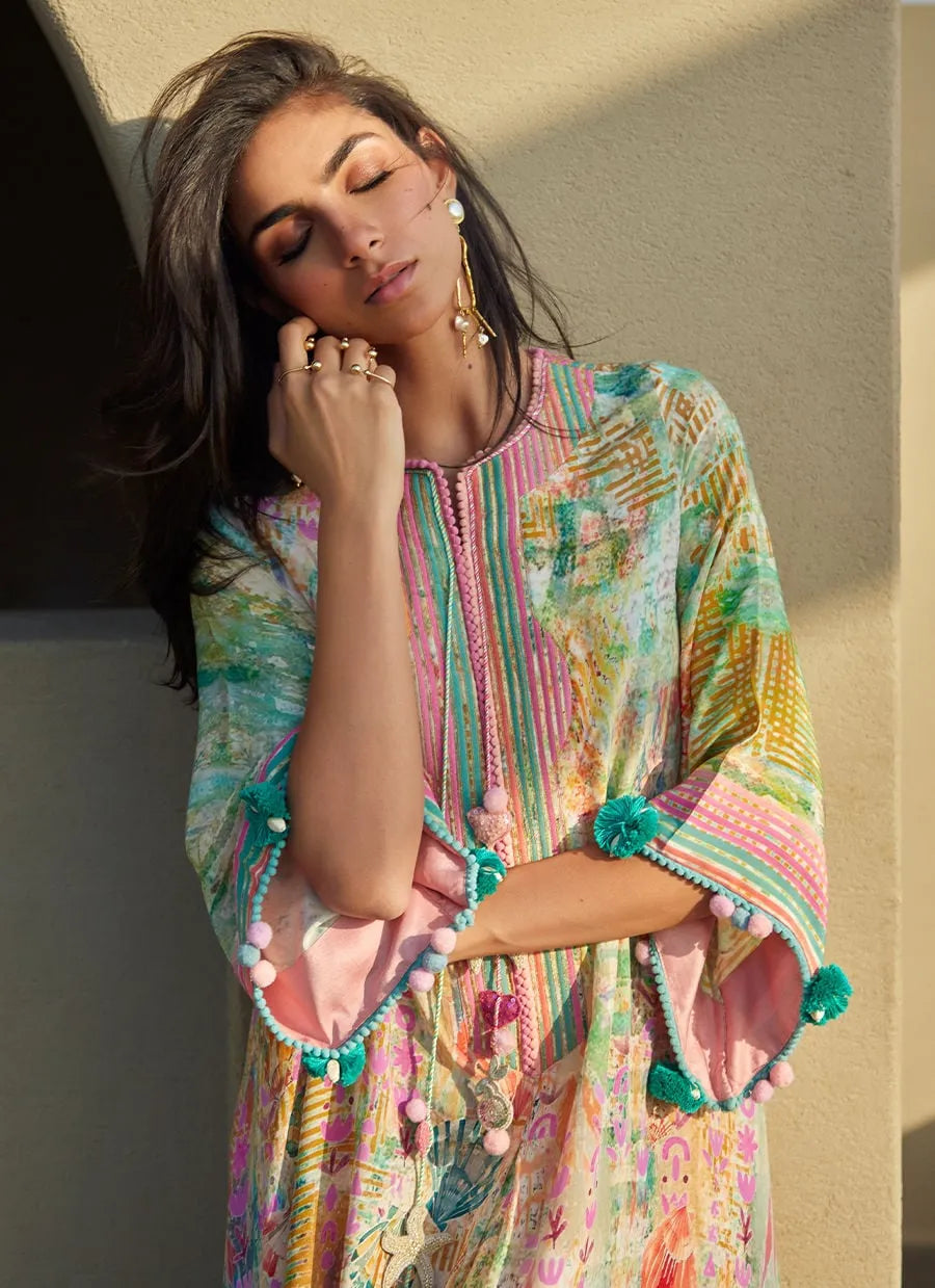 Woman wearing a colorful, patterned dress with pom-pom details against a neutral wall.
