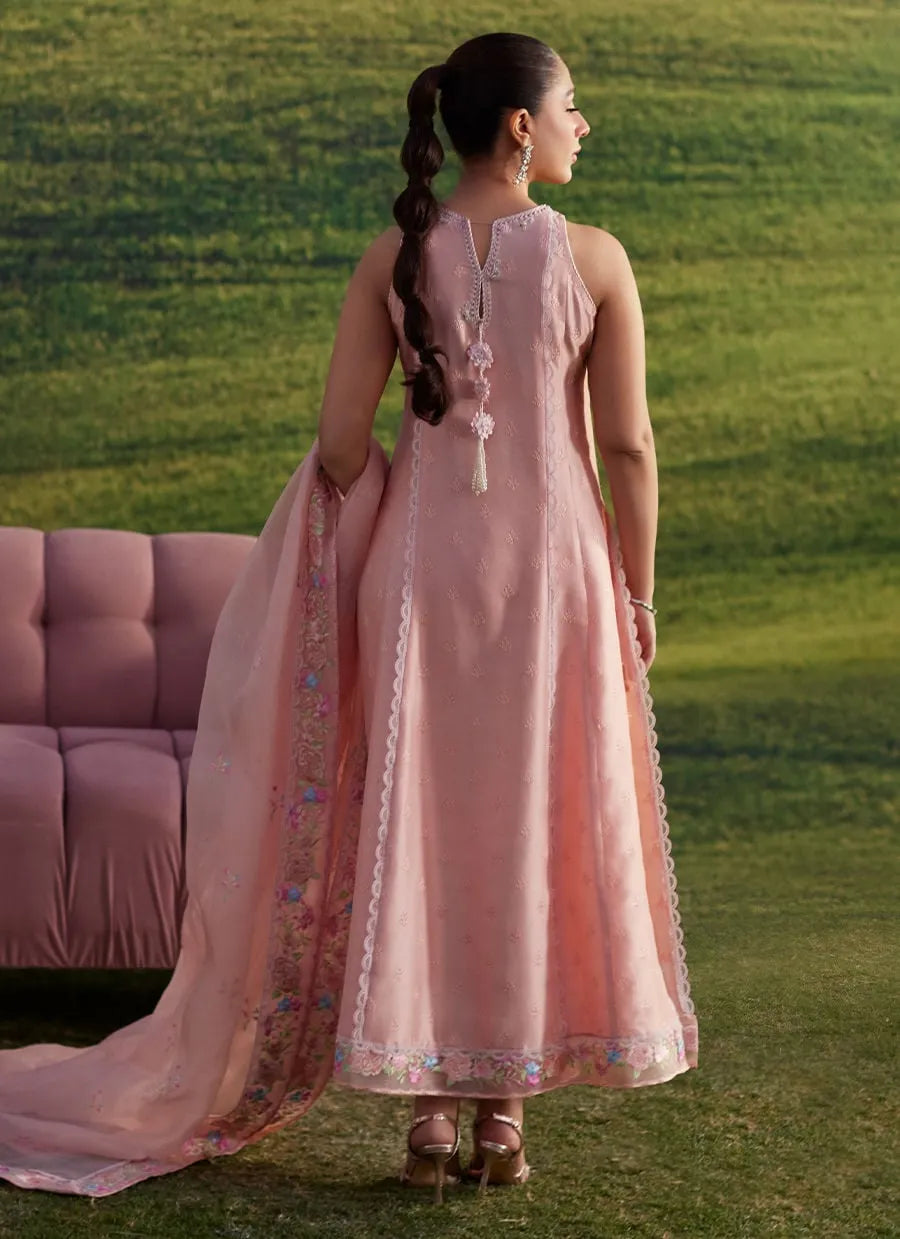 Woman in a pink traditional outfit standing on grass with a pink sofa in the background