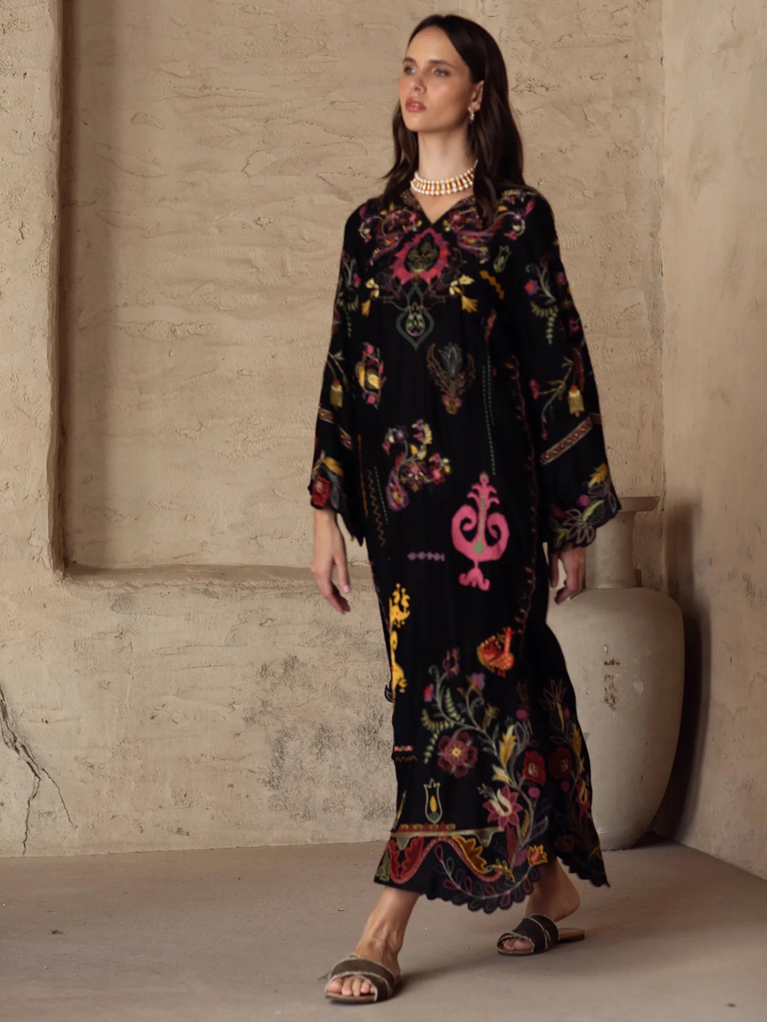 Woman wearing a black embroidered dress against a neutral wall.