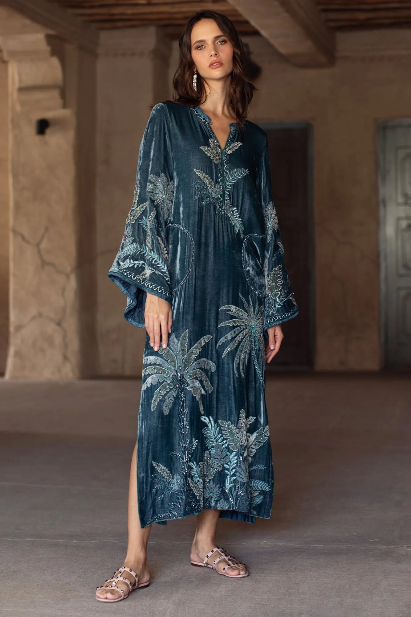 Woman wearing a blue embroidered dress in an indoor setting with beige walls.