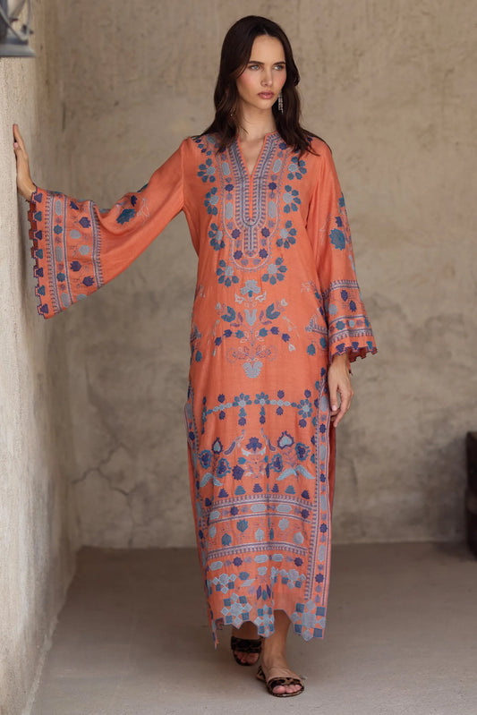 Woman wearing a long, patterned dress against a neutral wall.