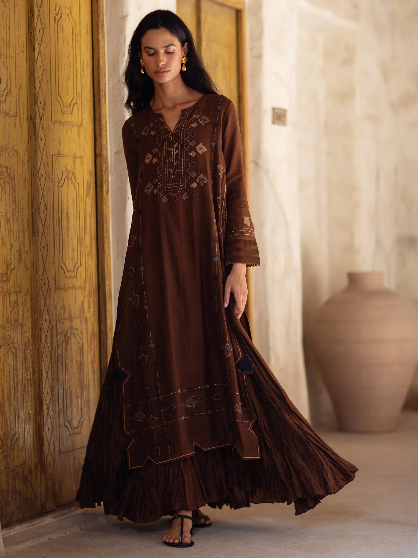 Woman wearing a long brown embroidered dress in an indoor setting.