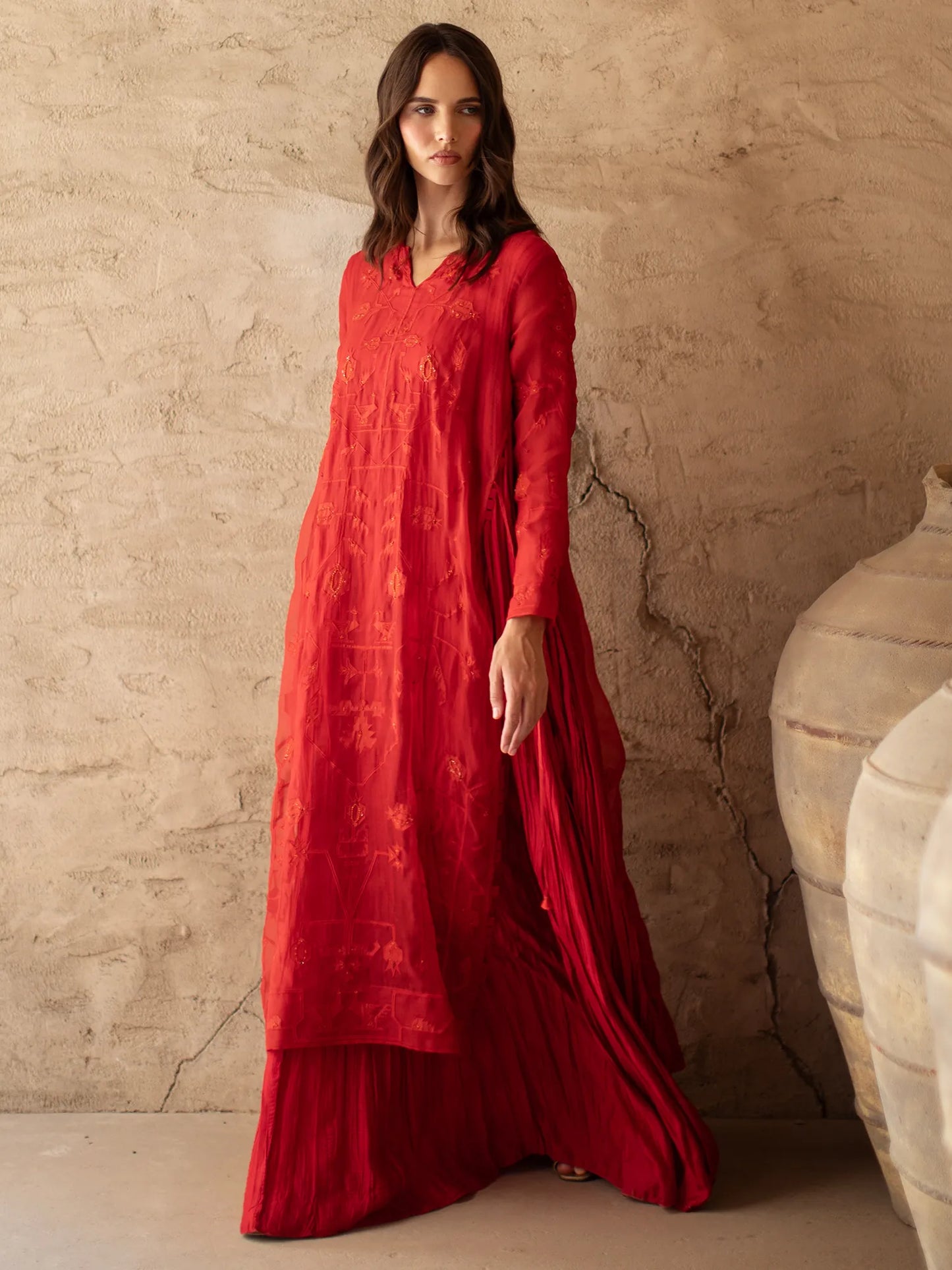 Woman wearing a red dress standing against a textured beige wall.