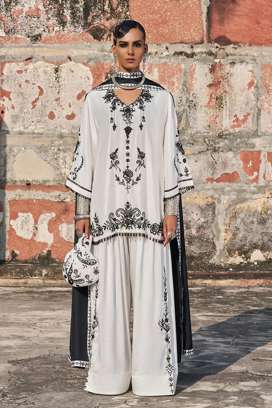 Woman in a white and black embroidered outfit standing against a textured wall.