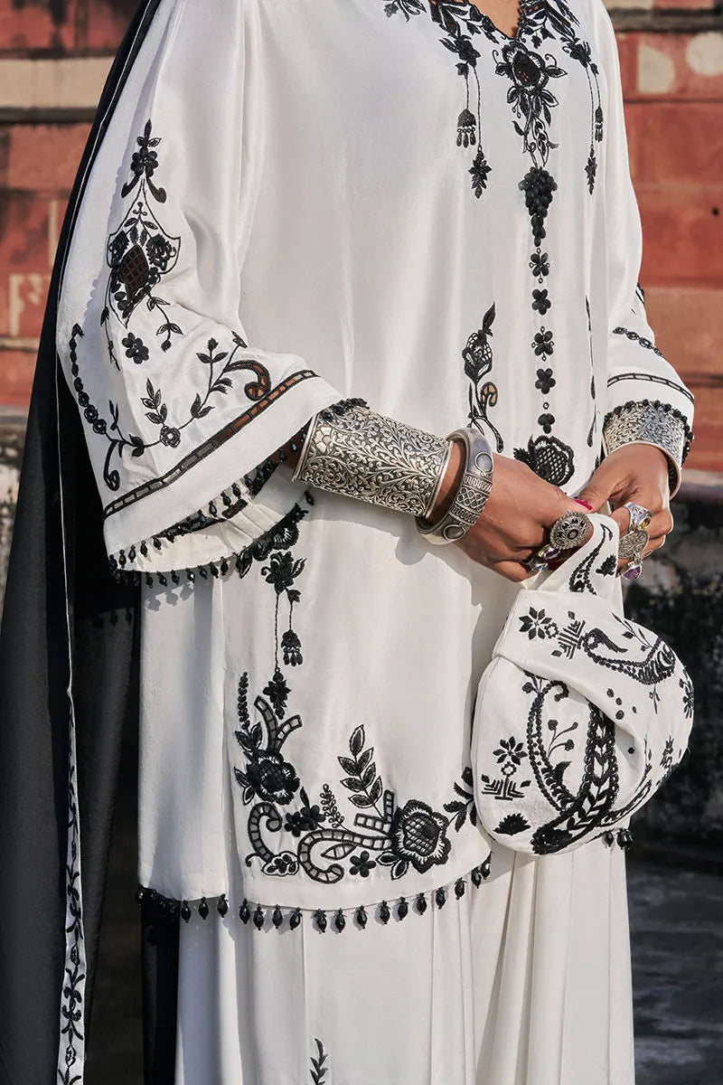 White outfit with black embroidery and a matching bag held by a person.