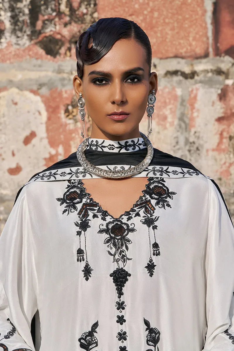 Woman wearing a white and black embroidered outfit with a textured wall background