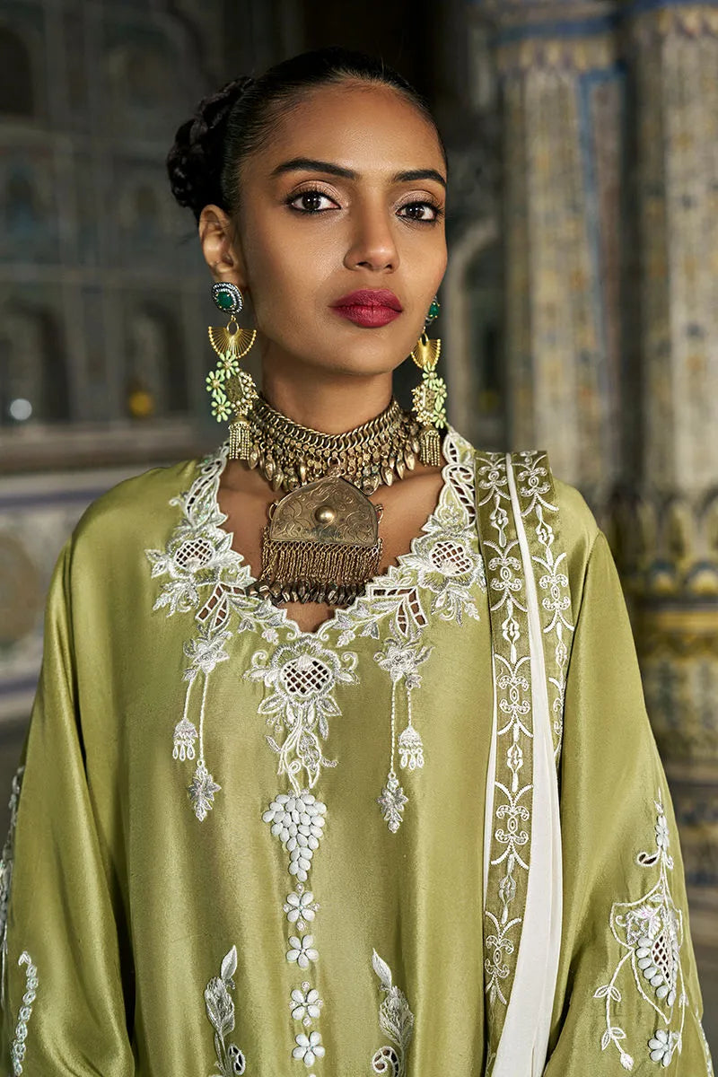 Woman wearing a green embroidered traditional outfit with jewelry in an indoor setting.