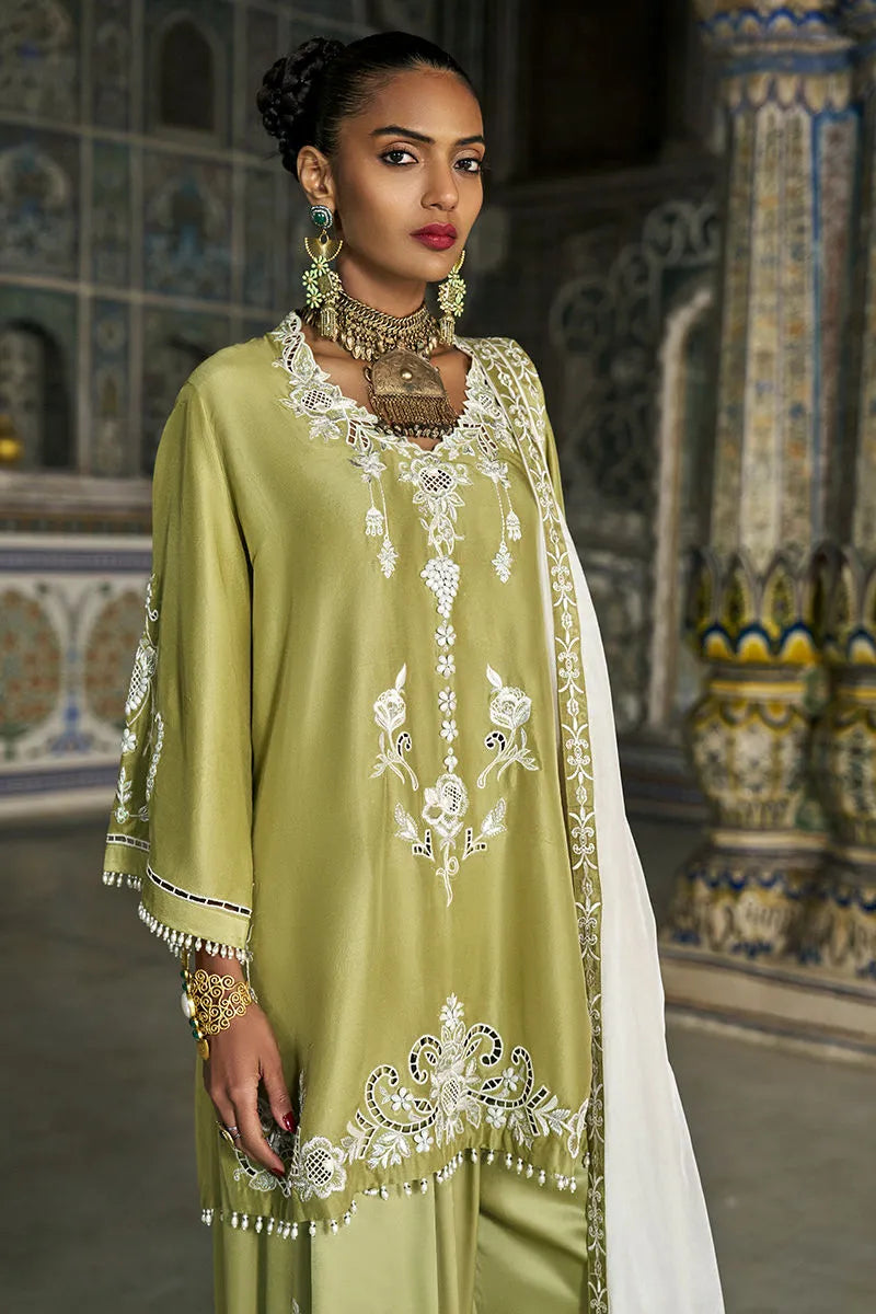 Woman in a green and white embroidered traditional outfit standing in an ornate interior setting.