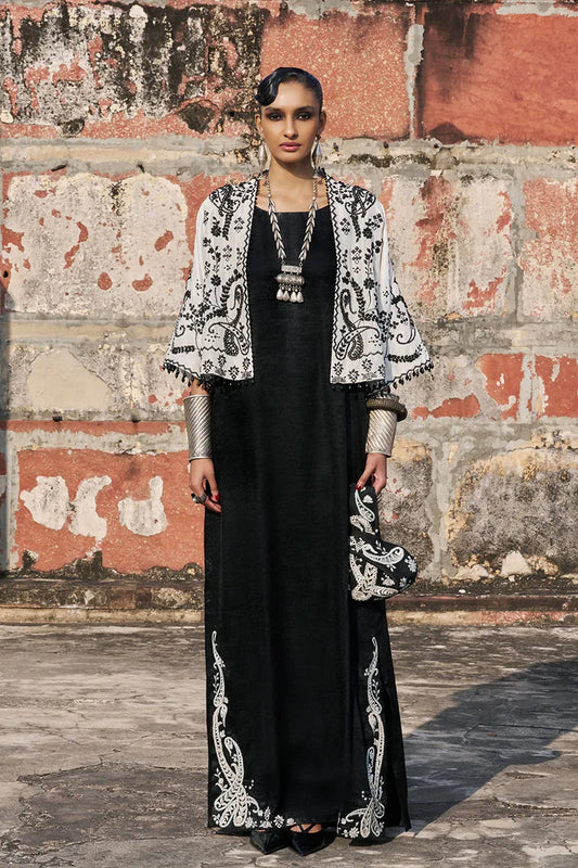 Woman in black dress with white embroidery standing against a textured wall.