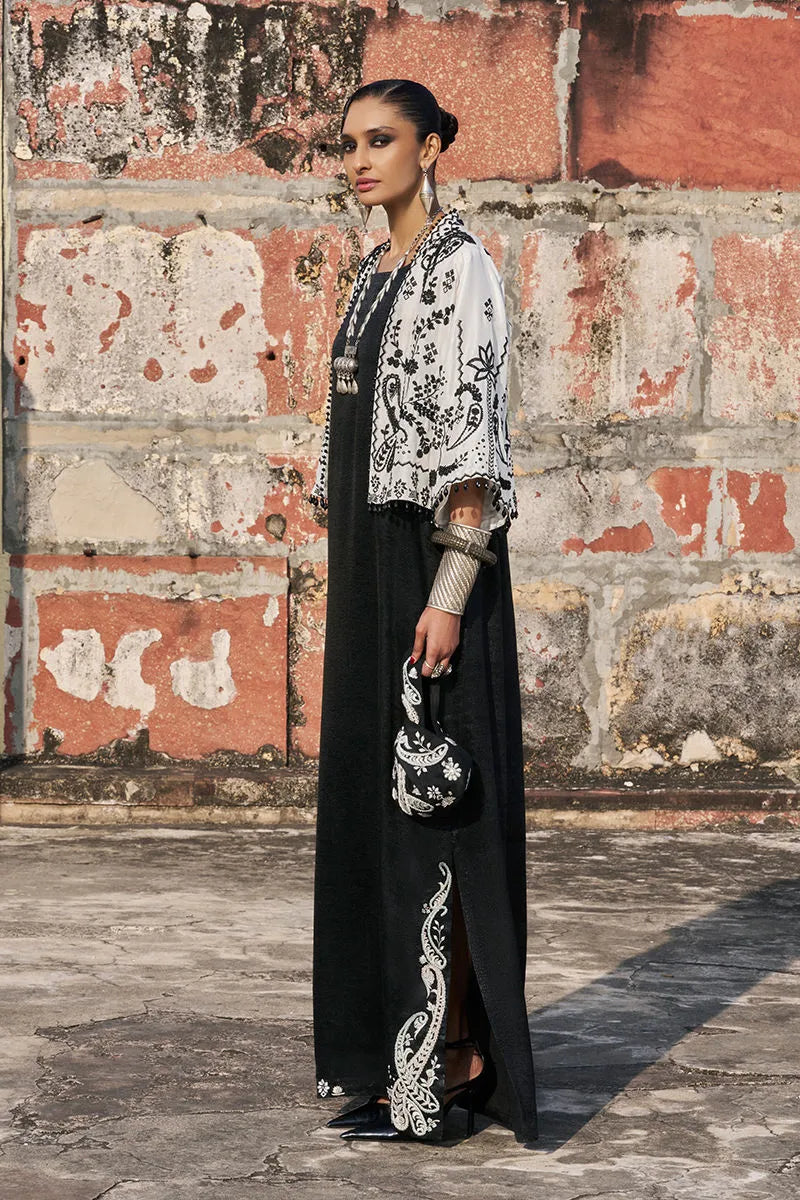 Woman in a black and white embroidered outfit standing against a textured wall.