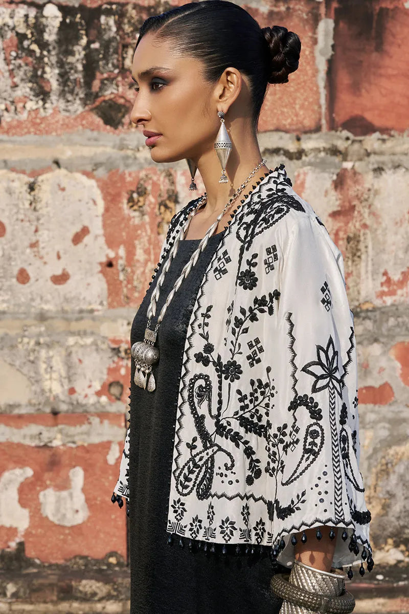 Woman wearing a black and white patterned shawl against a textured wall.