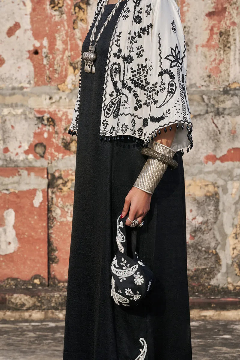 Person wearing a black outfit with white embroidery against a textured wall.