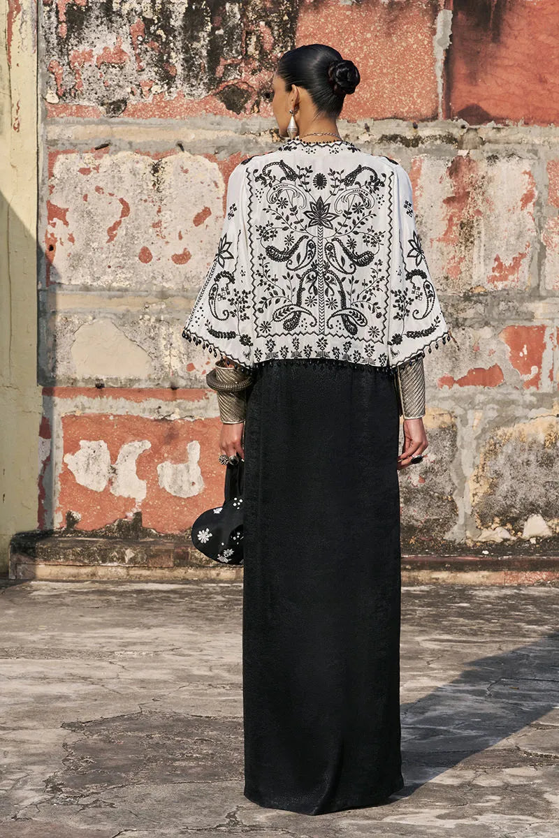 Person wearing a black and white embroidered jacket against a textured wall.