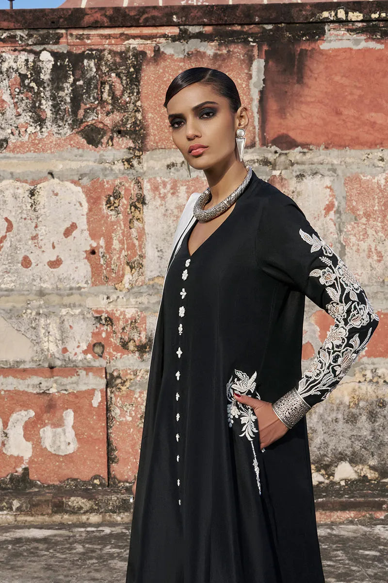 Woman wearing a black outfit with floral embroidery against a textured wall.