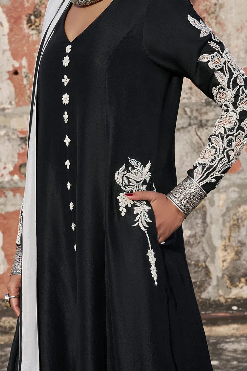 Black dress with white embroidery on sleeves against a textured wall background