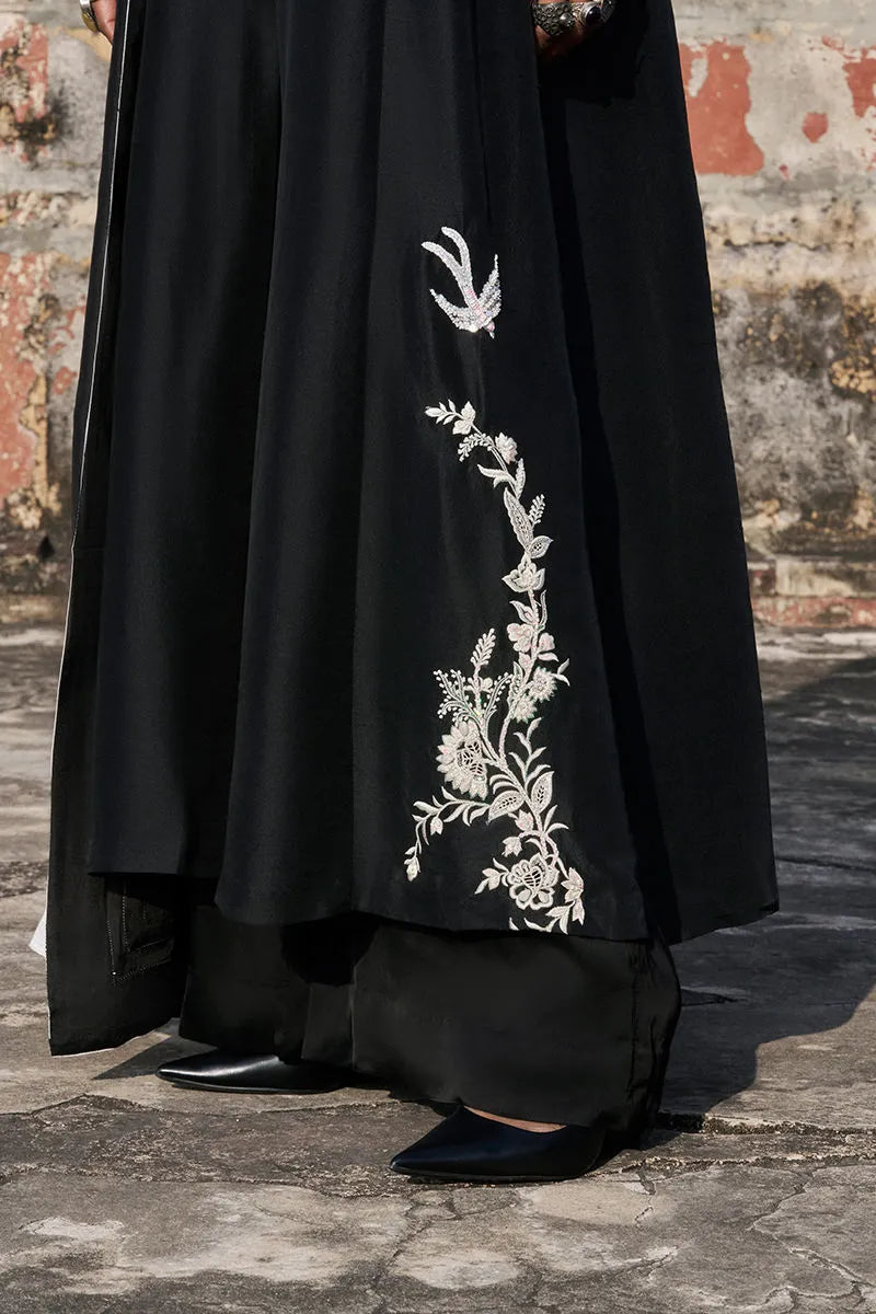 Black garment with white floral embroidery against a textured wall.