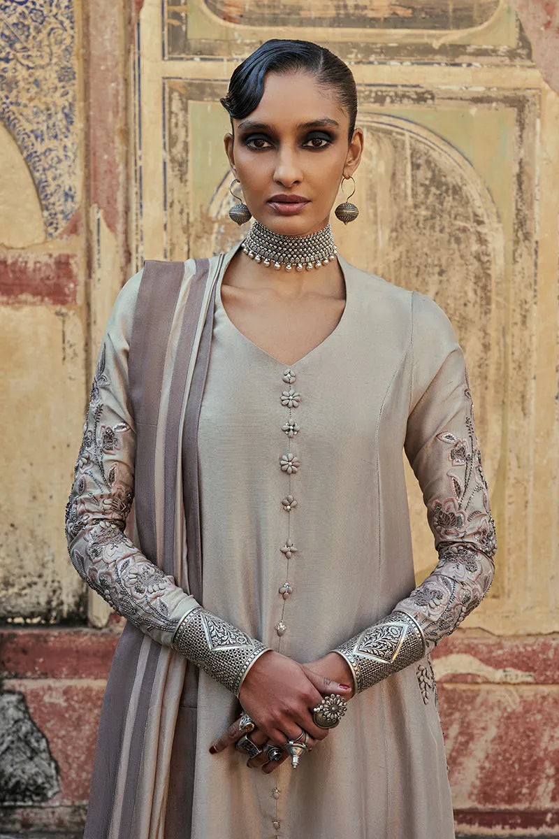 Woman in traditional attire standing in front of an ornate wall.