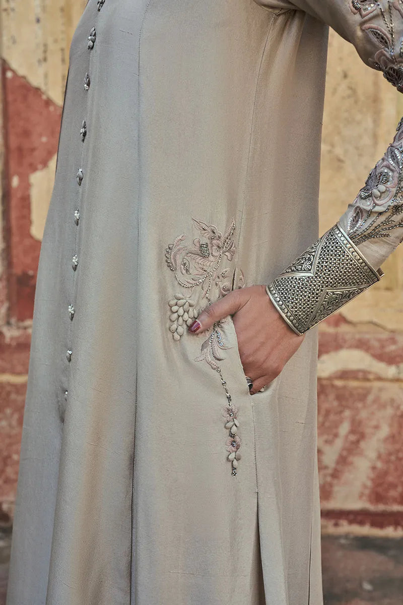 Close-up of a light gray traditional outfit with intricate embroidery against a textured wall.