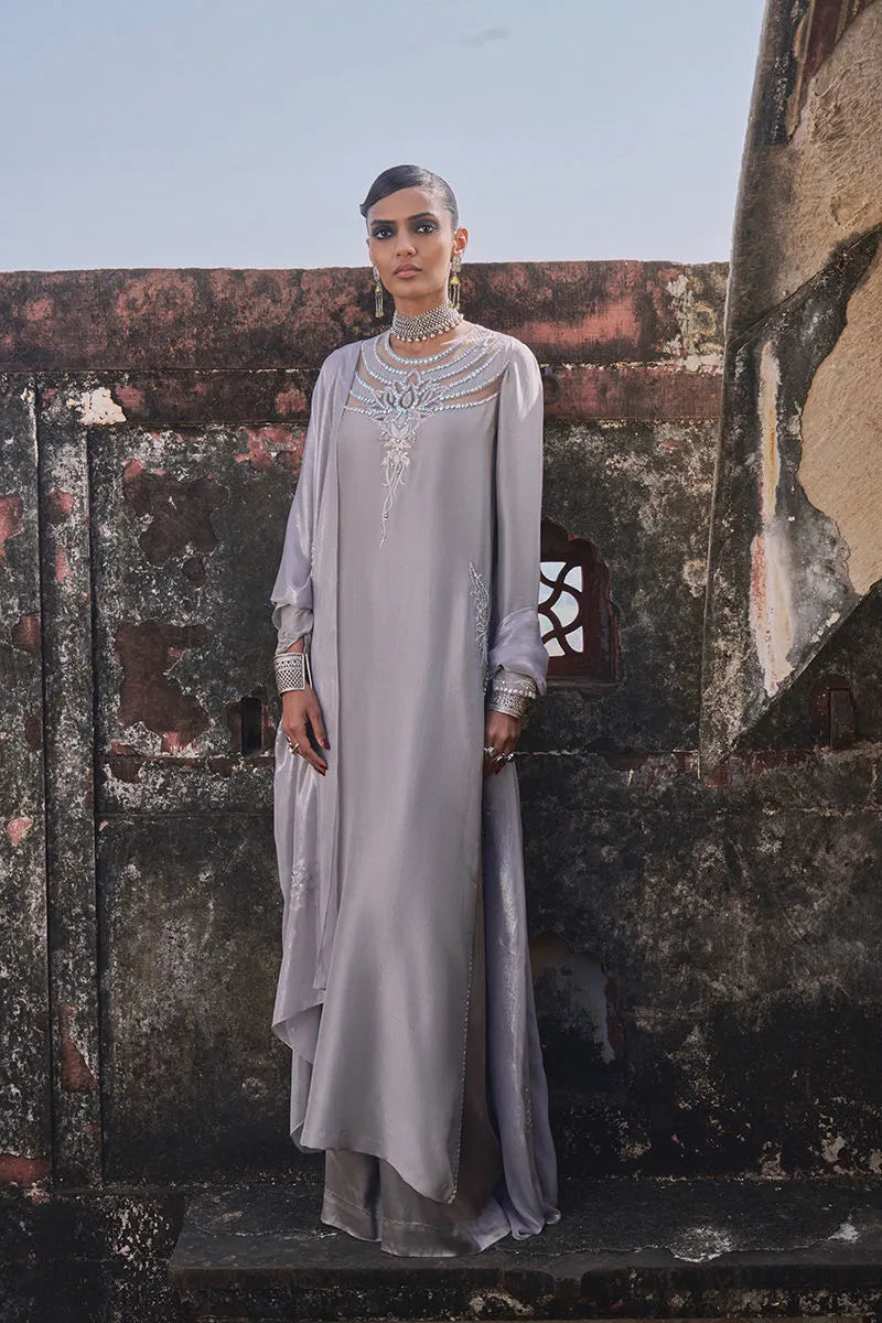 Woman in a silver dress standing against a textured wall.