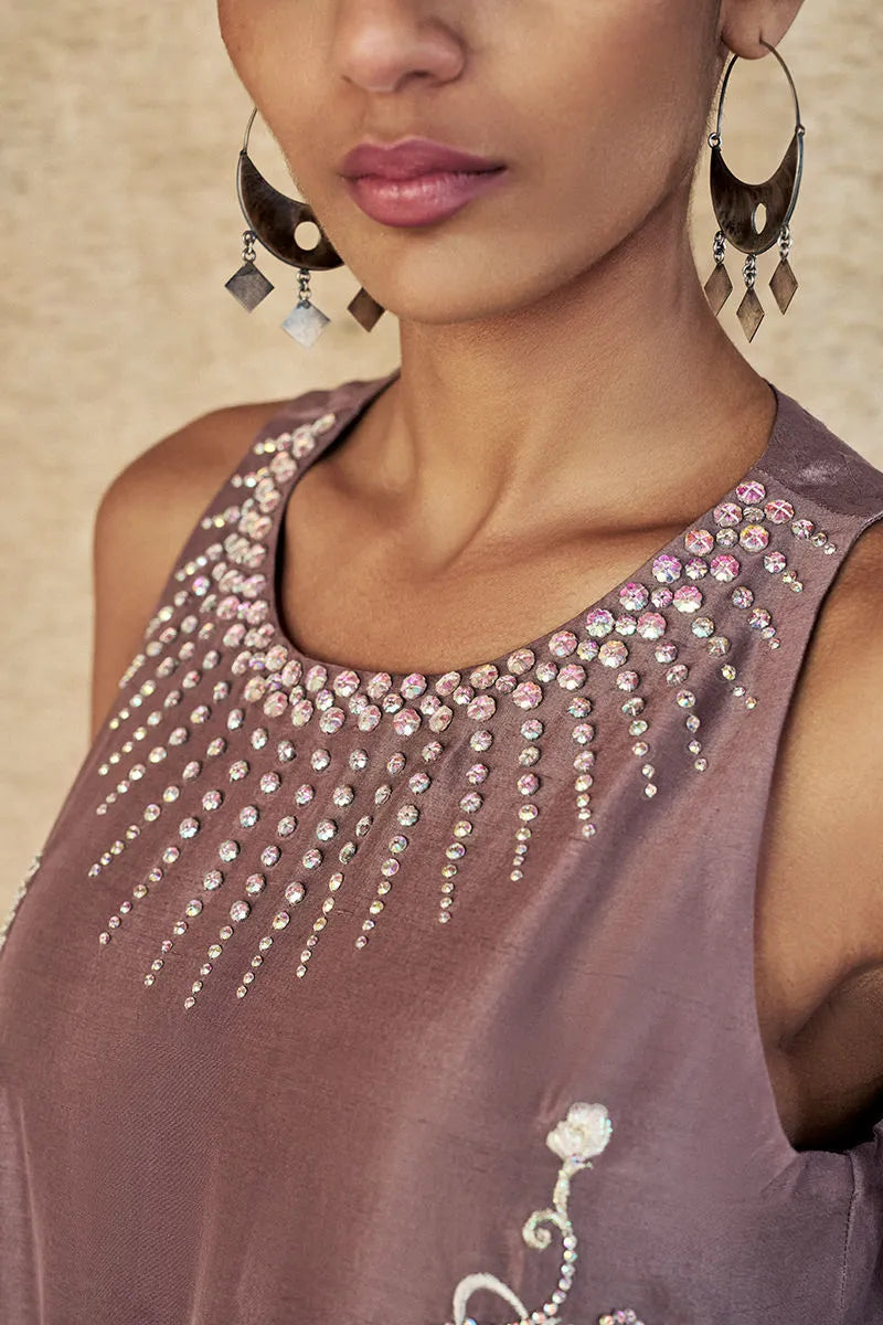 Close-up of a woman wearing a brown top with embellishments and earrings.