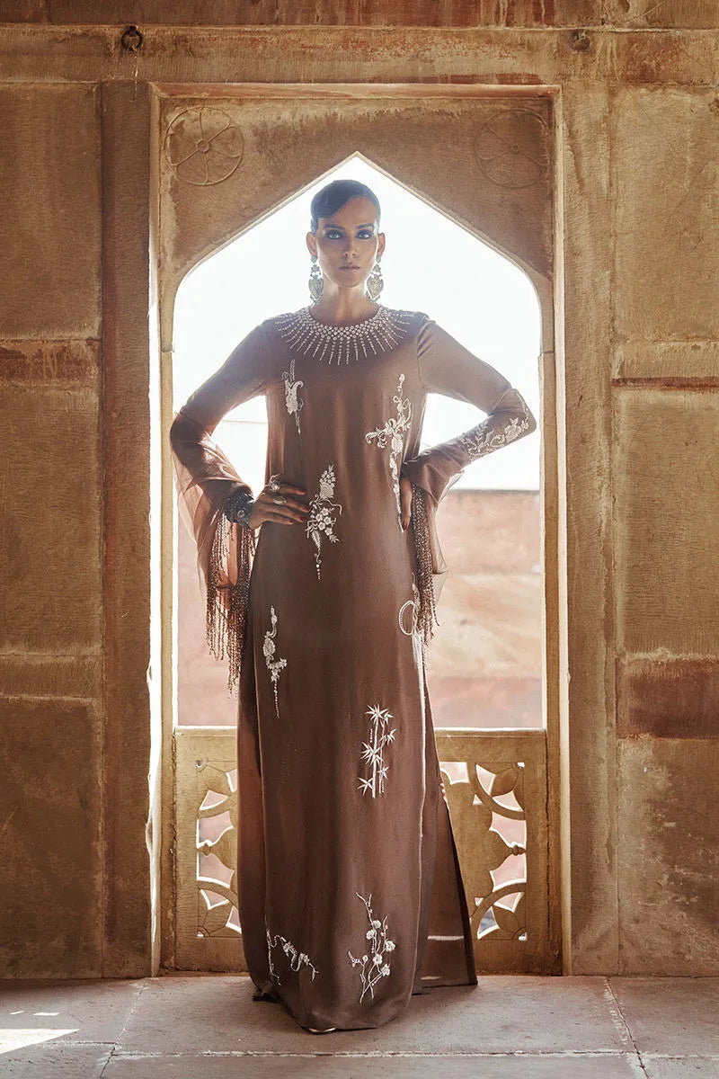 Woman in a long, dark brown dress with white patterns standing in an archway.