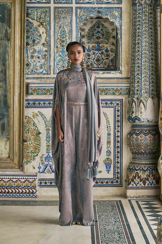 Woman in a long, light-colored dress standing in a room with ornate, colorful tilework.