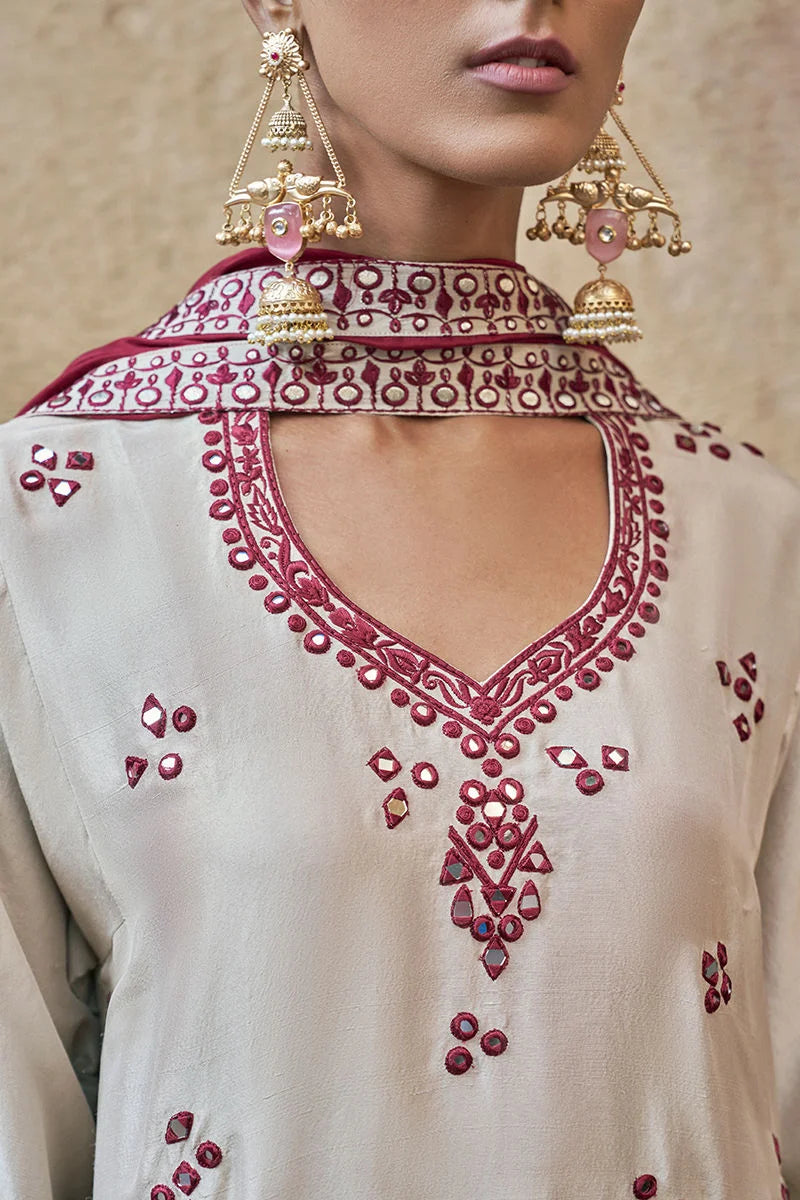 Close-up of a person wearing a white embroidered top with red details and gold jewelry.