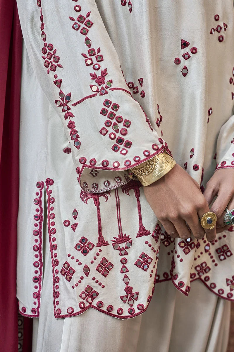 Close-up of a white garment with red embroidery and gold accents.