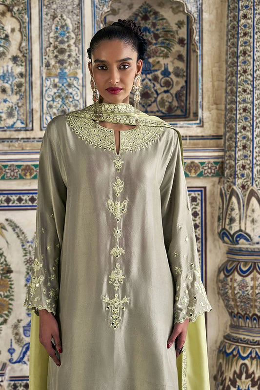 Woman wearing a light green embroidered dress in front of a decorative wall.